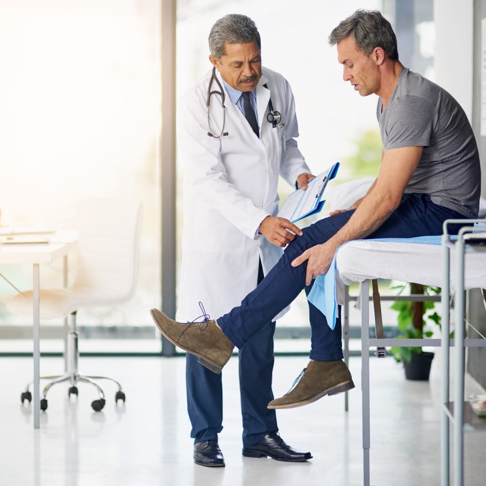 Shot of a mature doctor examining his patient who is concerned about his knee